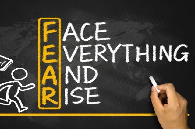 Fear of the blank page expressed through the words “Face Everything and Rise” on a chalkboard, encouraging writers to begin anyway.