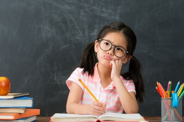 Fear of the blank page shown by a child holding a pencil and thinking hard over a blank notebook, unsure of what to write.
