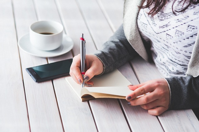 Art print business disclaimer represented by a woman writing in a journal beside coffee and a phone.
