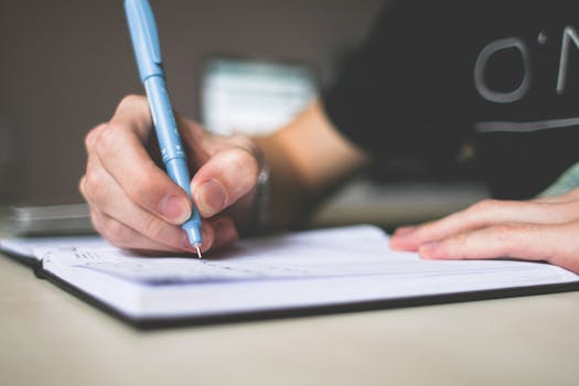 Person writing in a journal, representing reflection and personal responsibility in the art business disclaimer. Close-up of hand writing in notebook using a blue pen, focus on creativity.