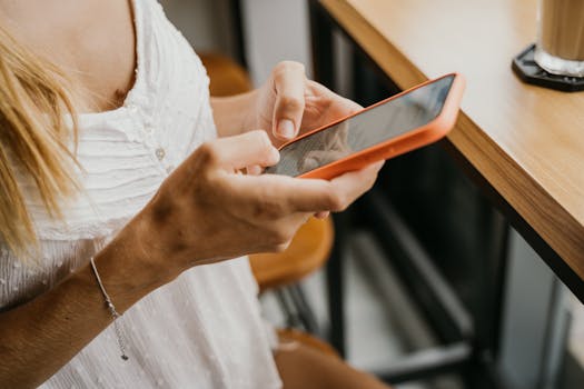 Woman using smartphone while reading an art journaling disclaimer page, viewing the privacy policy section, at a wooden table in an indoor cafe setting.