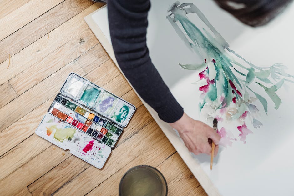 Art print business privacy policy represented by an artist painting watercolor flowers beside a palette. A creative top view of an artist painting with vibrant watercolors on paper.